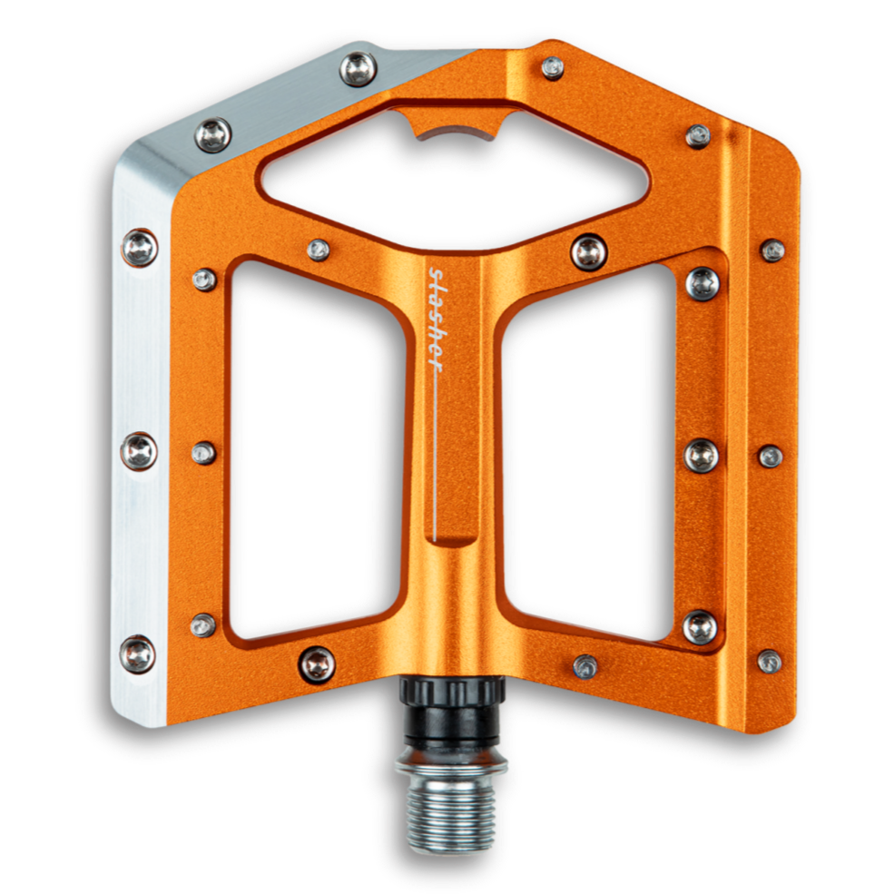 An orange Cube Slasher flat pedal with a silver CNC-machined aluminium body and Cr-Mo axle, featuring chamfered edges and adjustable pins.